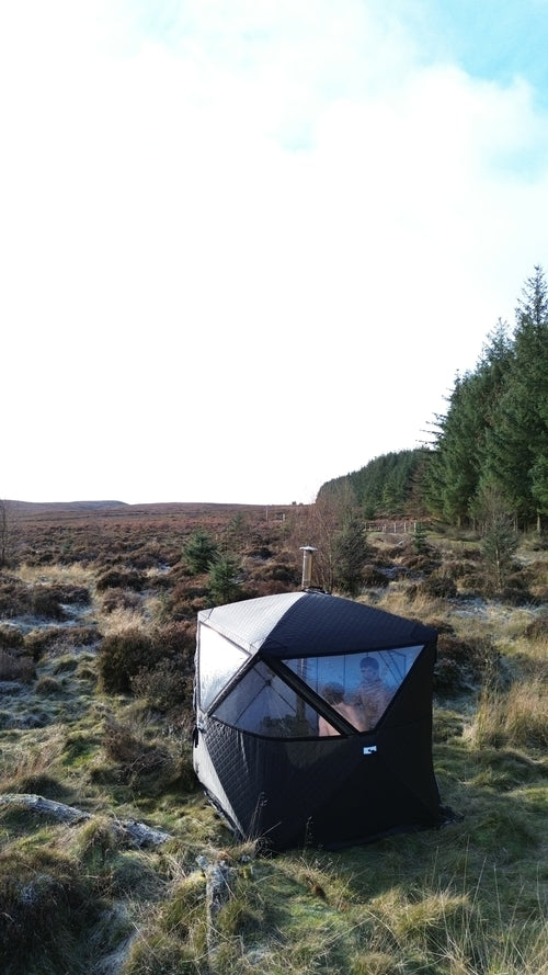 Black and white tent pitched on a grassy hillside with trees in the background